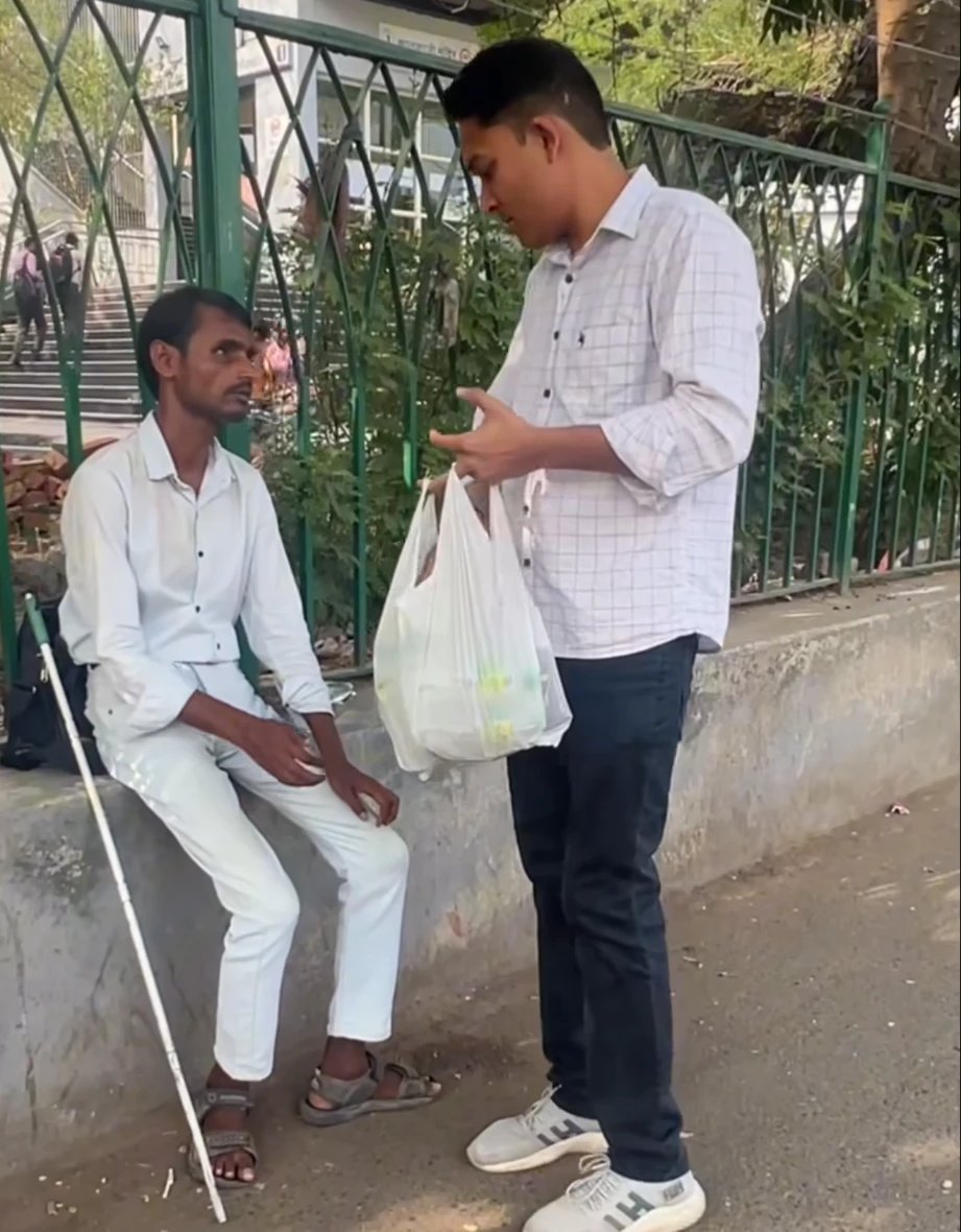 Our volunteer handing a bag of seva items to a visually impaired man by the road